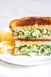 stacked tuna melt with spinach on a plate with chips.