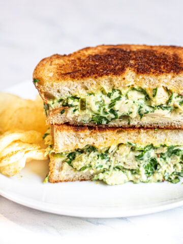 stacked tuna melt with spinach on a plate with chips.