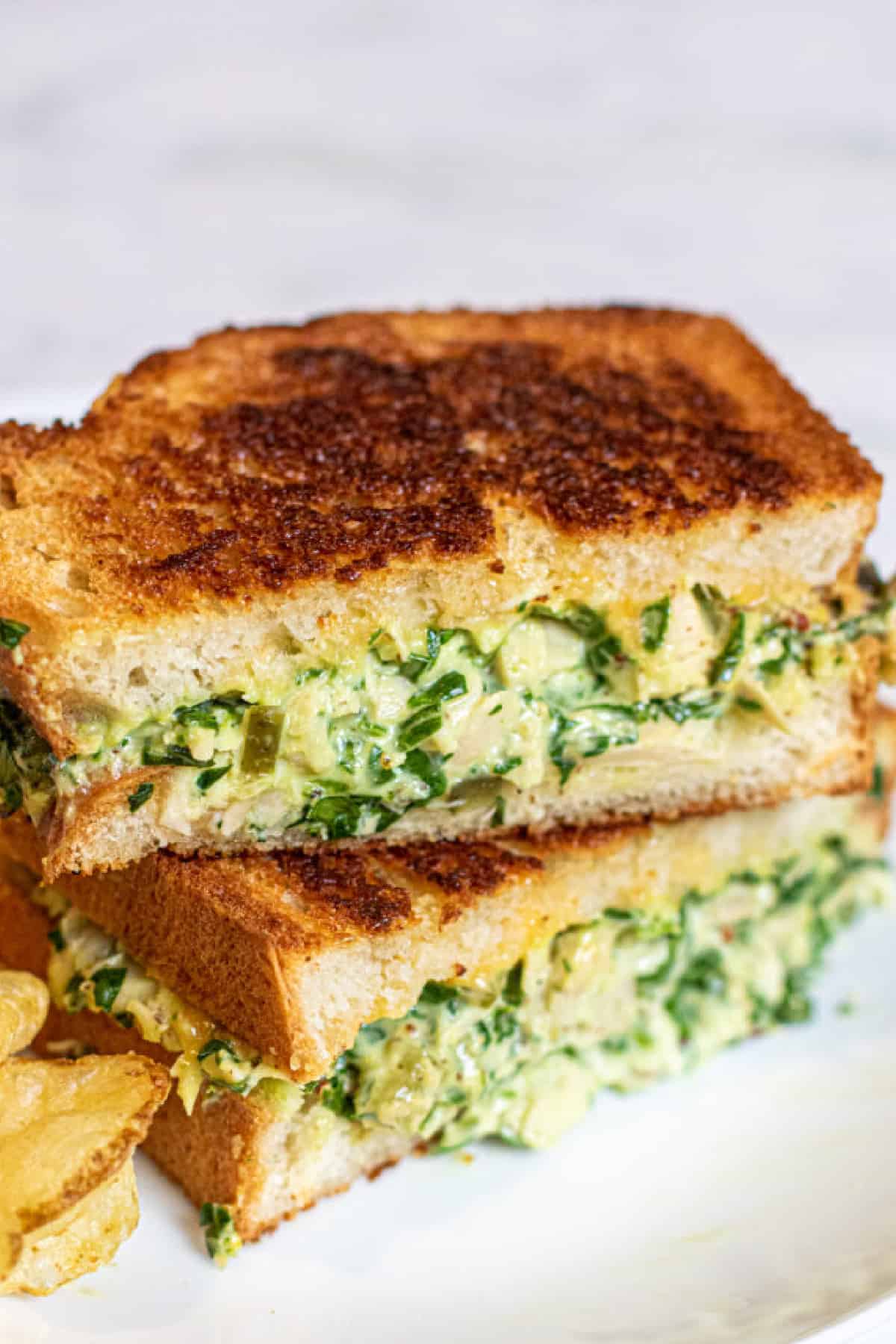 stacked tuna melt with spinach on a plate with chips.