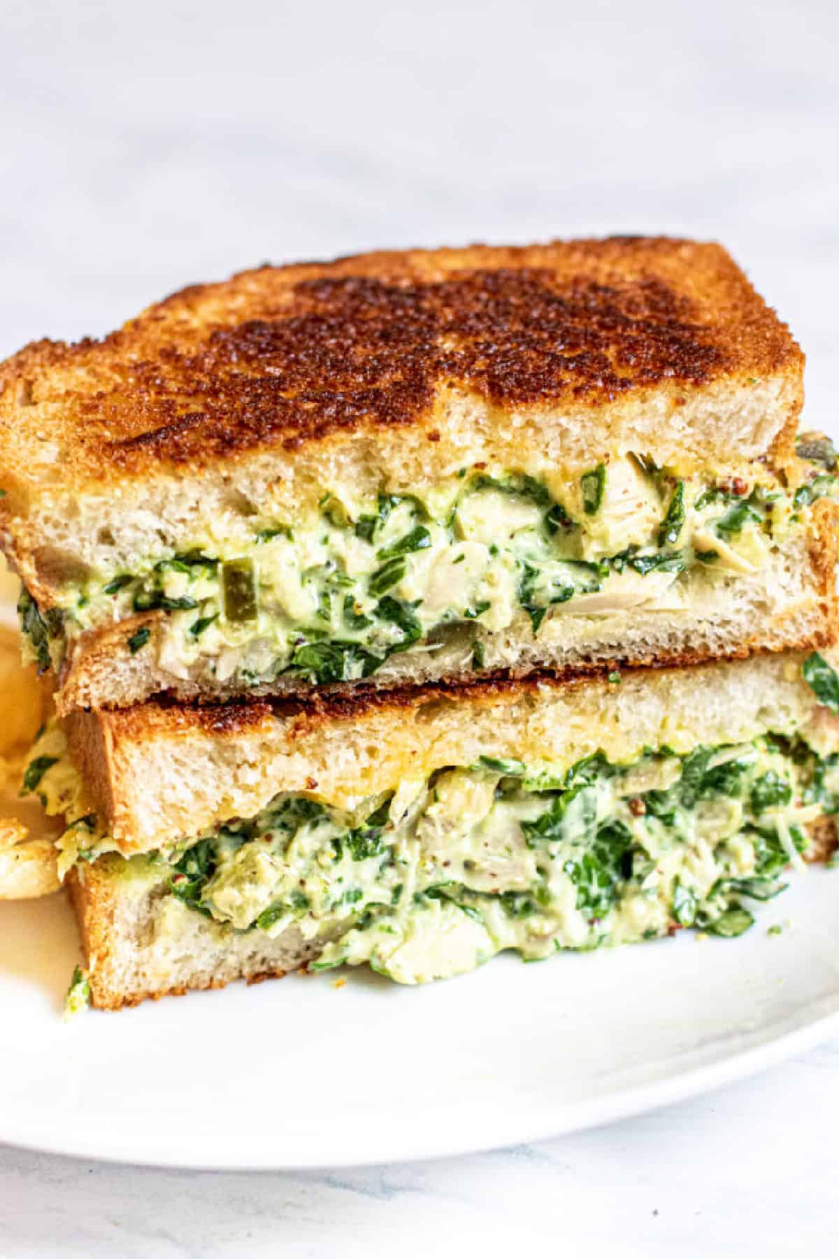stacked tuna melt with spinach on a plate with chips.