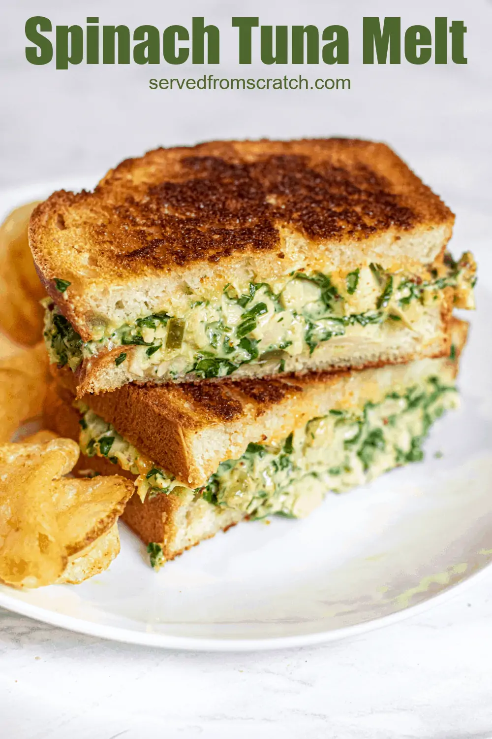 stacked tuna melt with spinach on a plate with chips.