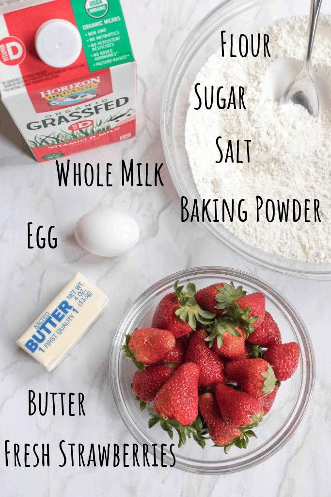 milk, bowl of flour and sugar, egg, strawberries and butter on counter
