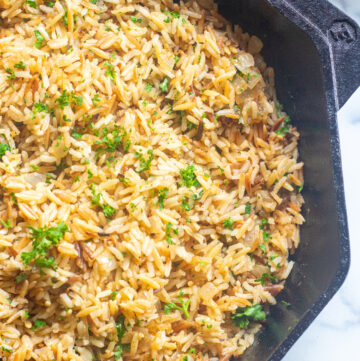 a cast iron with cooked rice pilaf and parsley.