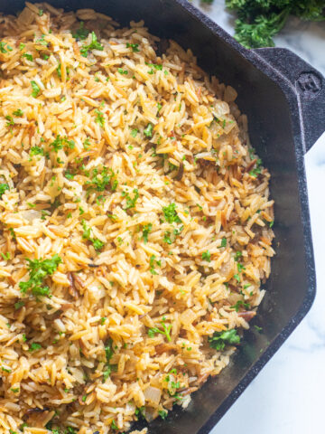 a cast iron with cooked rice pilaf and parsley.