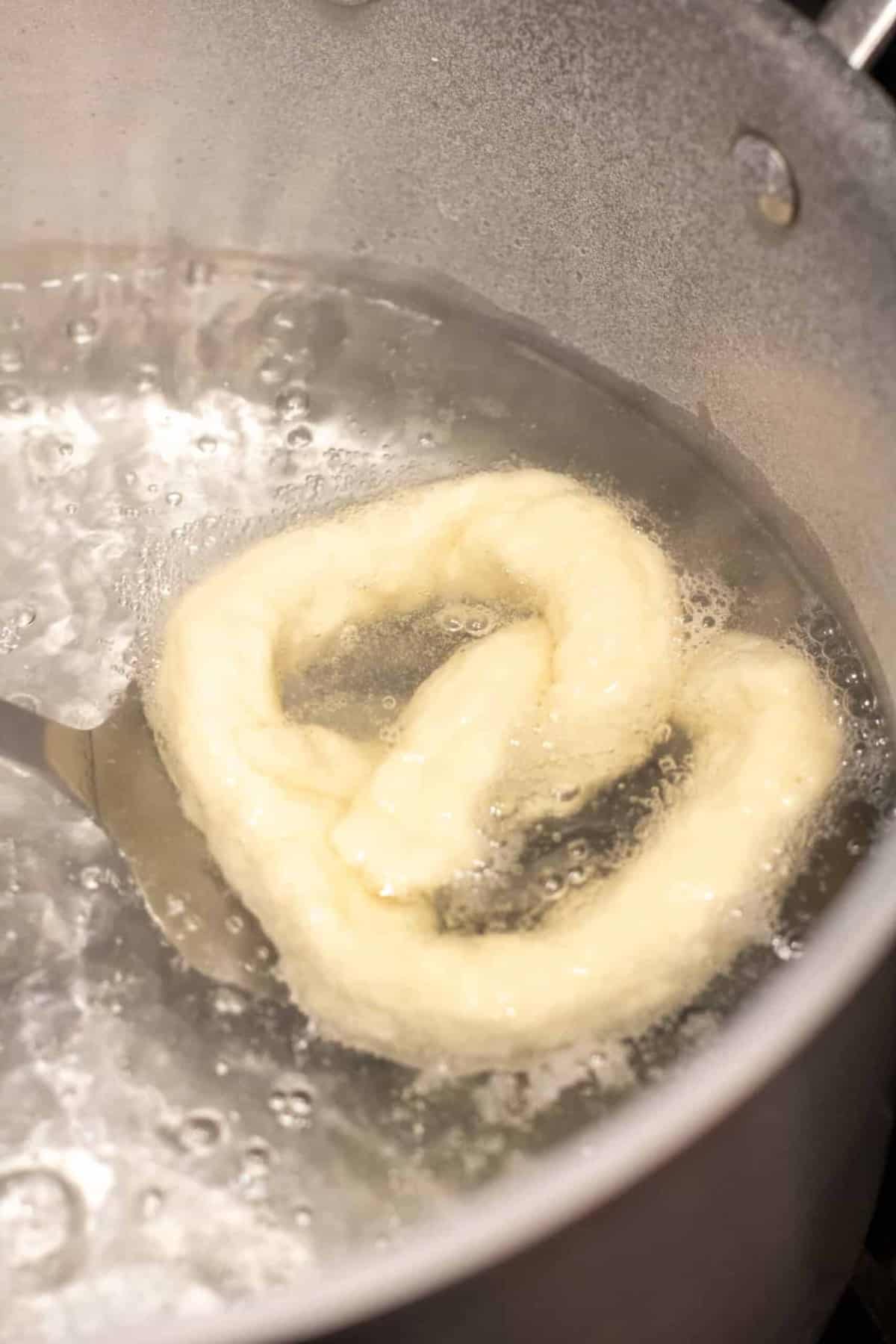 a raw pretzel in a pot of boiling water.