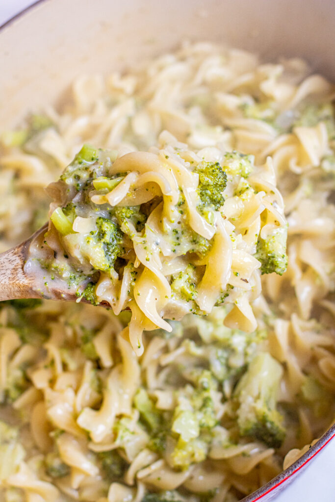 a wooden spoon holding some creamy pasta and broccoli