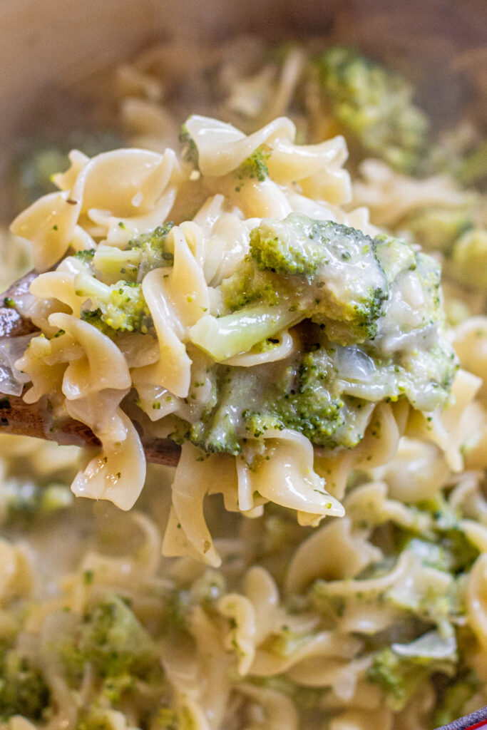 a wooden spoon holding some creamy pasta and broccoli