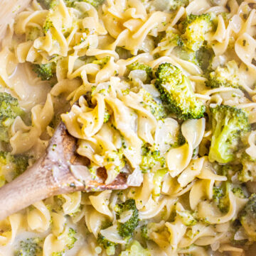 overhead of a wooden spoon in a creamy pot of pasta with broccoli