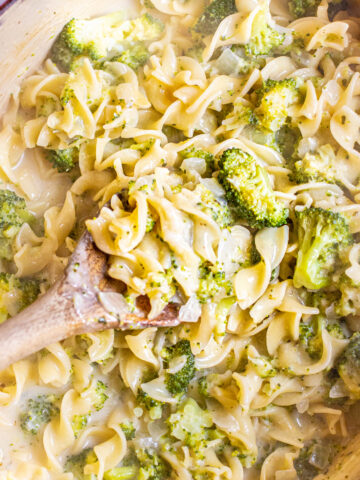 overhead of a wooden spoon in a creamy pot of pasta with broccoli