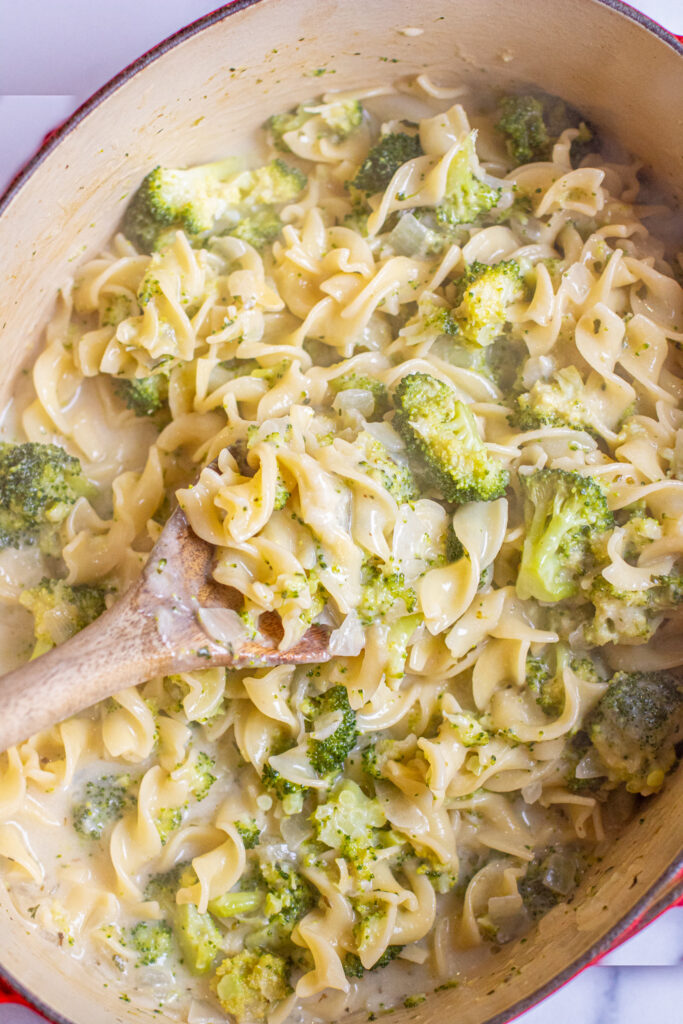 overhead of a wooden spoon in a creamy pot of pasta with broccoli.