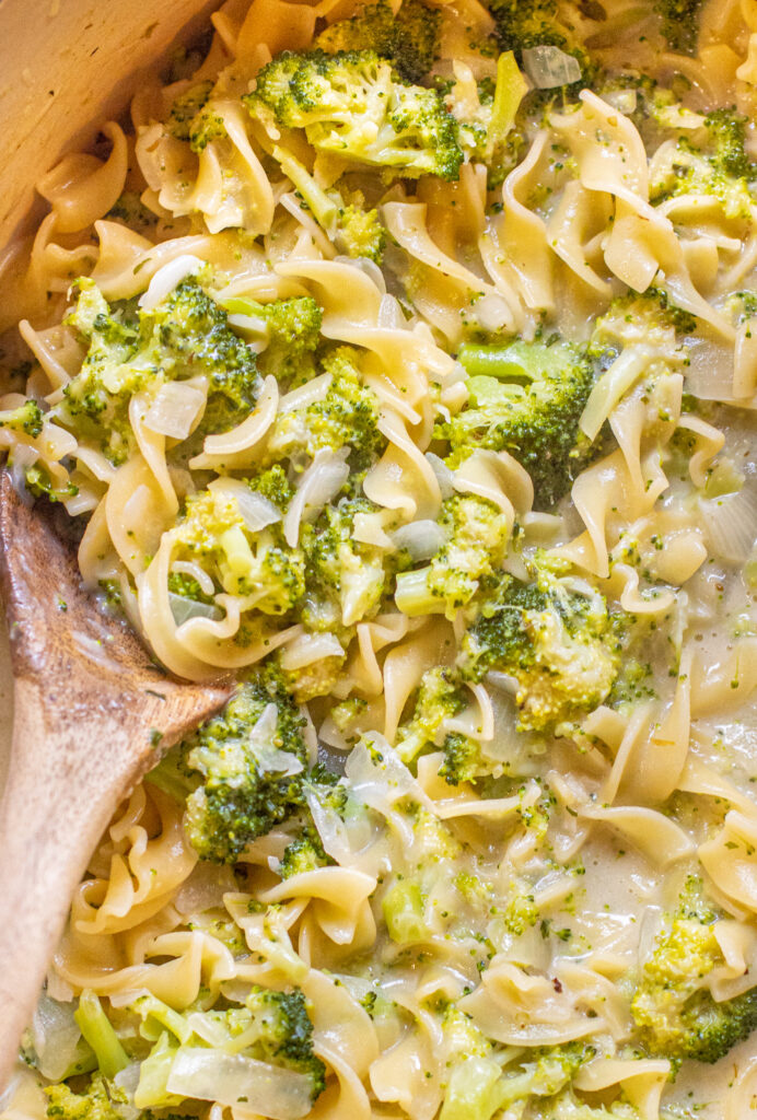overhead of a wooden spoon in a creamy pot of pasta with broccoli