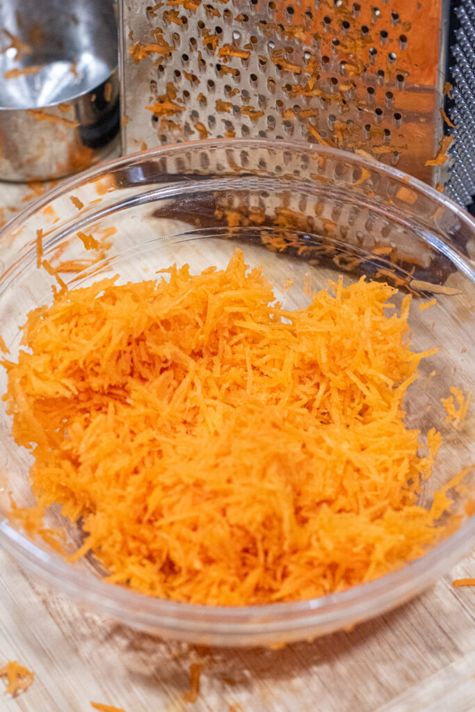 shredded carrots in a bowl and a grater.