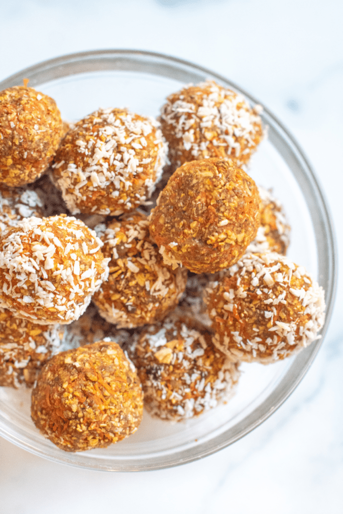 a bowl of balls of oats and carrots with some coated with coconut and some not.