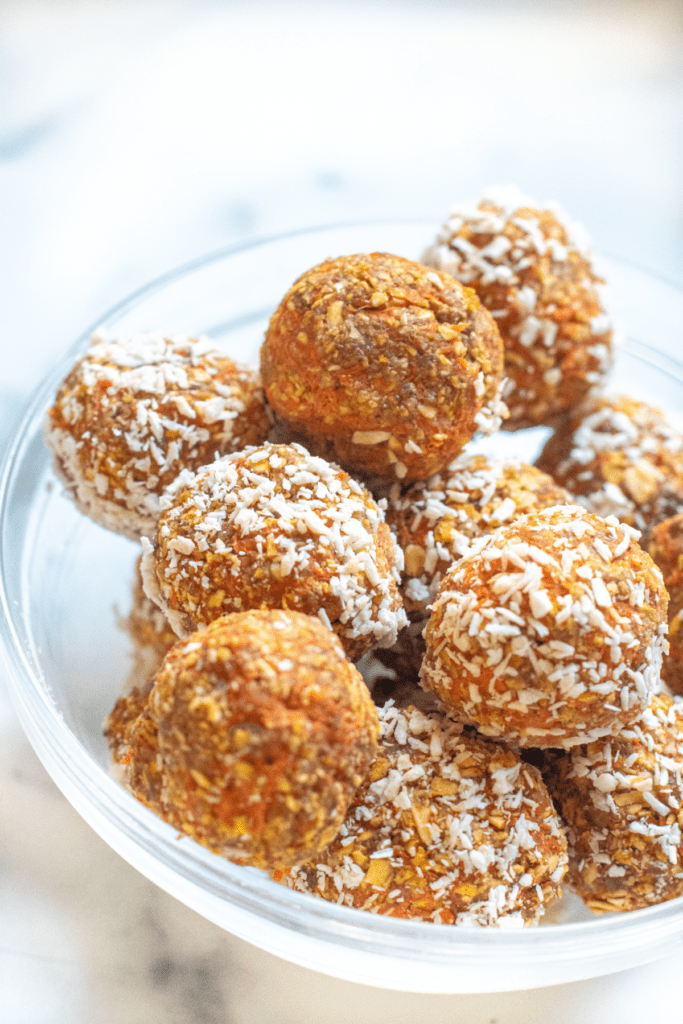a bowl of balls of oats and carrots with some coated with coconut and some not.