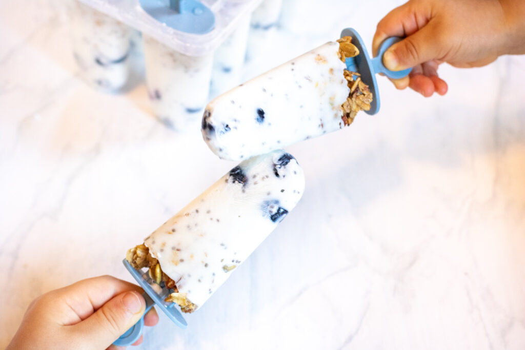 two kids holding yogurt popsicles touching.