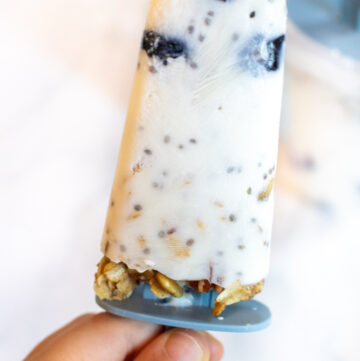 a hand holding a popsicle with blueberries and granola.