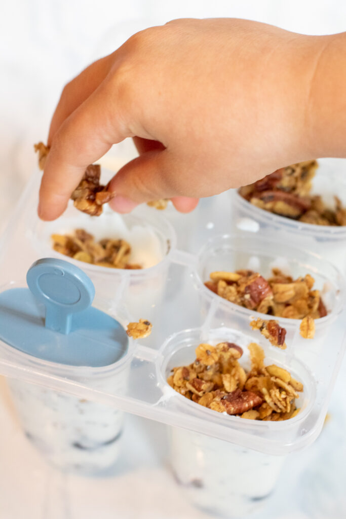 a hand putting granola into popsicles.