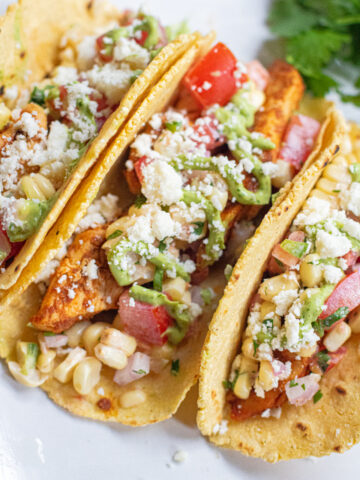 a plate of 3 corn tortilla tacos topped with crumbled cotija cheese.