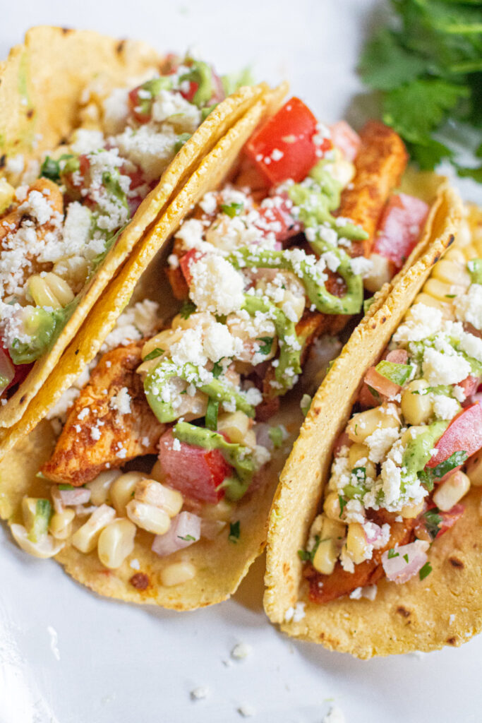 a plate of 3 corn tortilla tacos topped with crumbled cotija cheese.