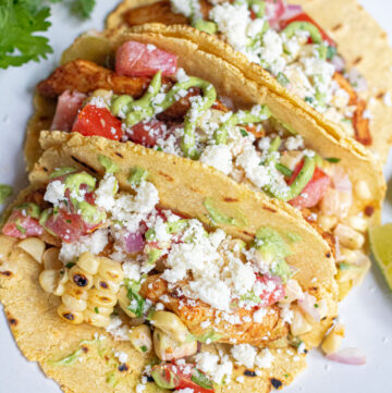 a plate of 3 corn tortilla tacos topped with crumbled cotija cheese.