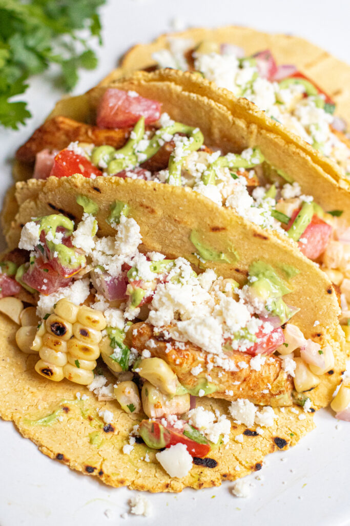 a plate of 3 corn tortilla tacos topped with crumbled cotija cheese.