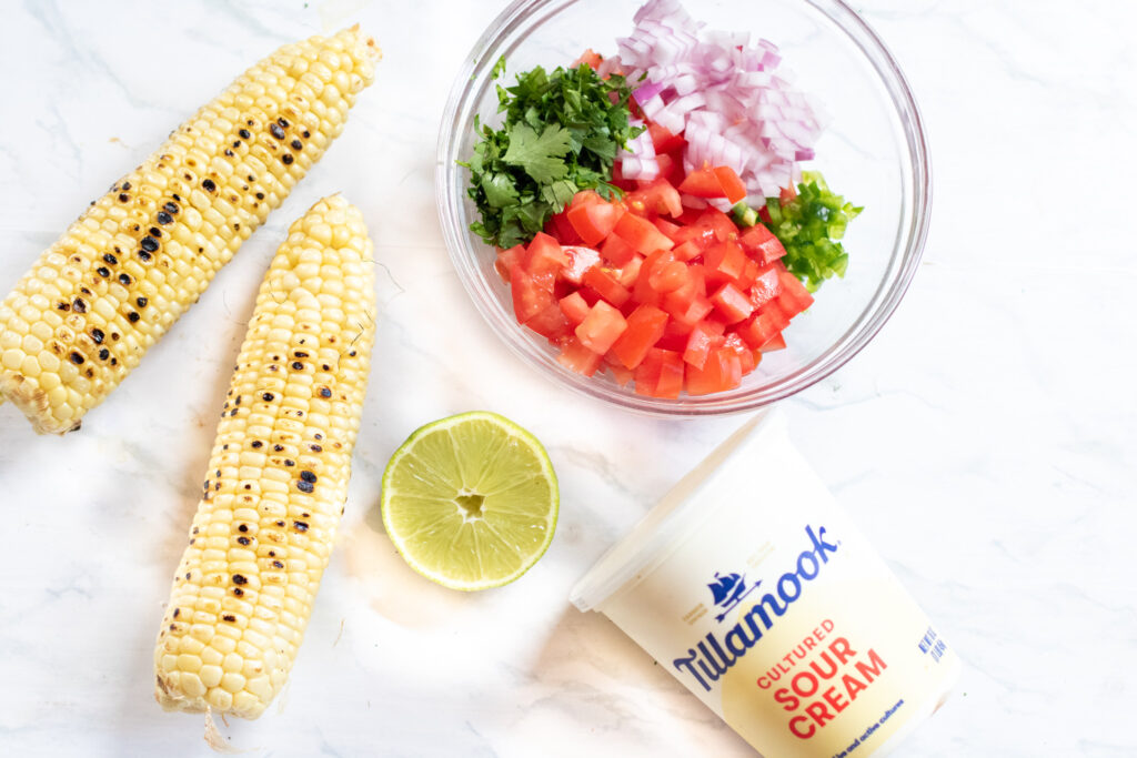 grilled corn with a bowl of tomatoes, onion, and lime and sour cream.