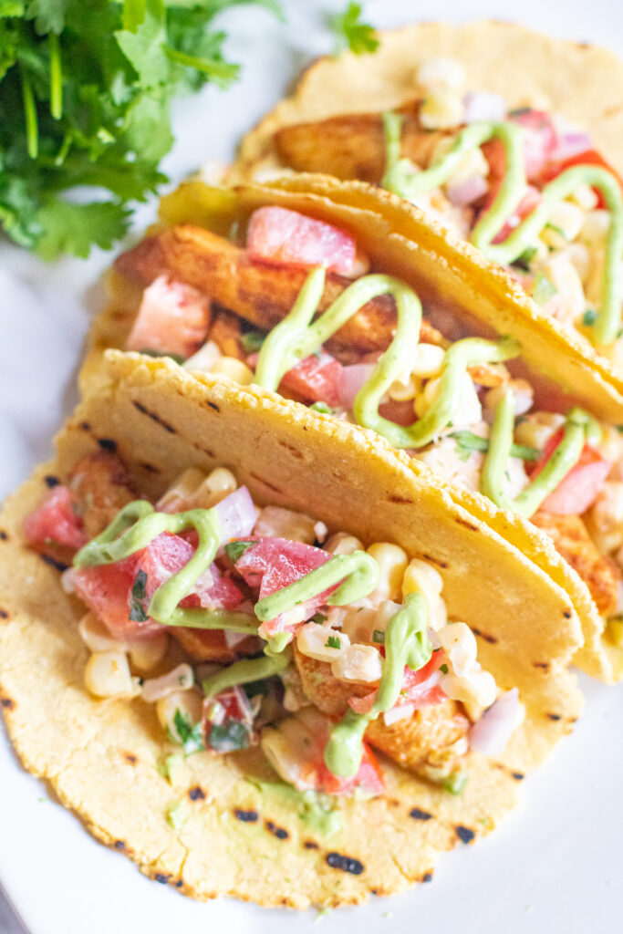 corn tacos with chicken, corn, tomatoes, and a drizzle of avocado cream.