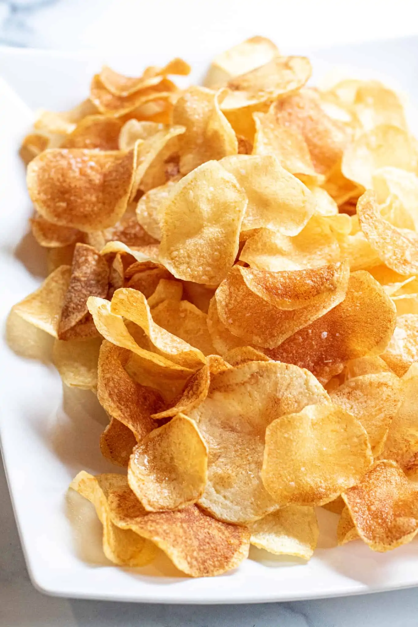 A plate of thin crispy potato chips. Sides for sandwiches. Sides for pulled pork sandwiches.
