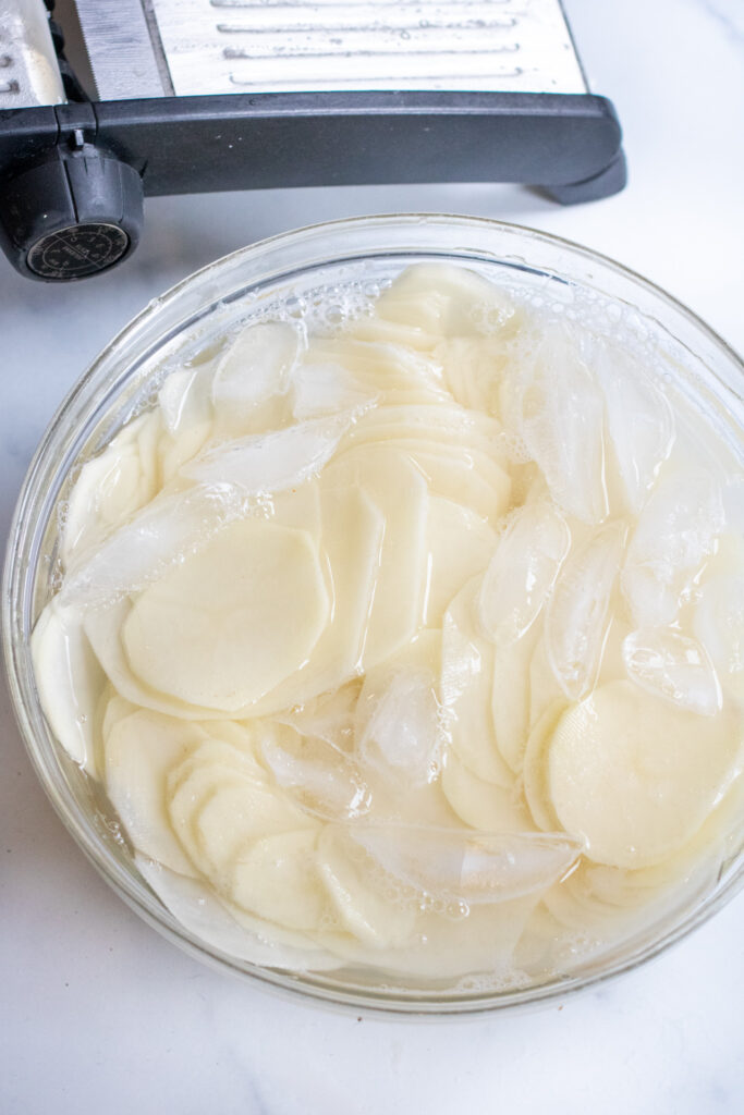 a bowl of ice water and thin potato slices. 