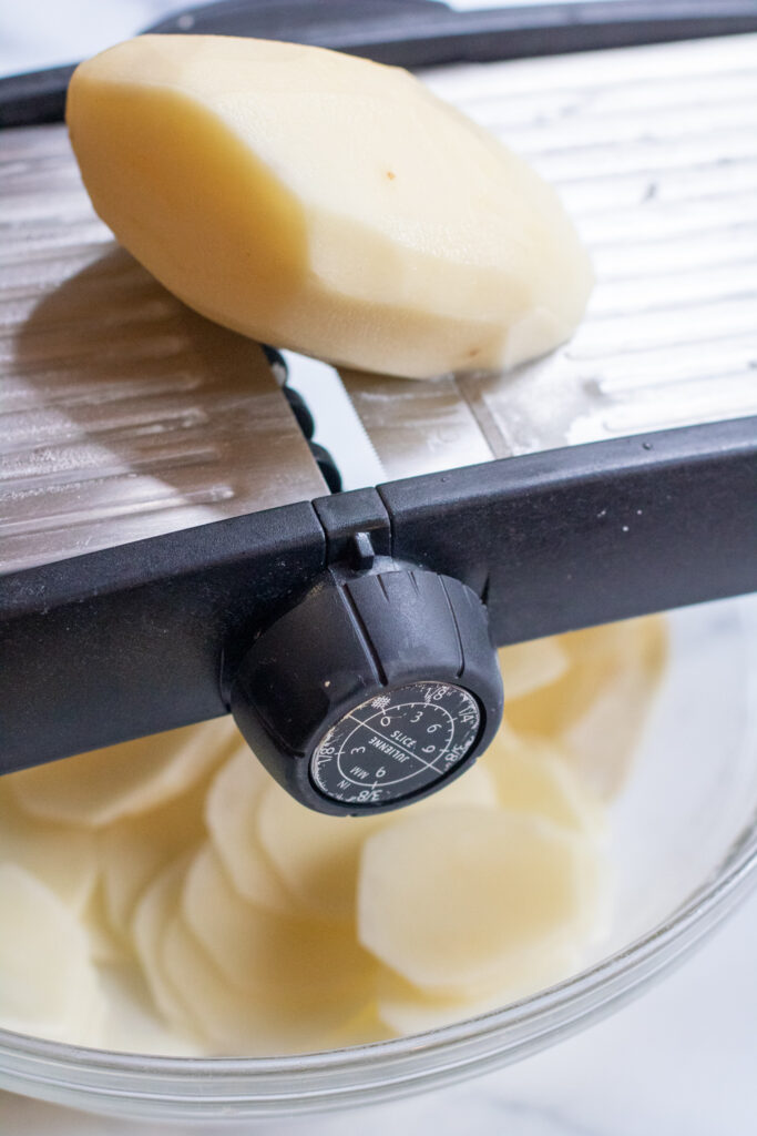 potato being sliced by a mandoline.