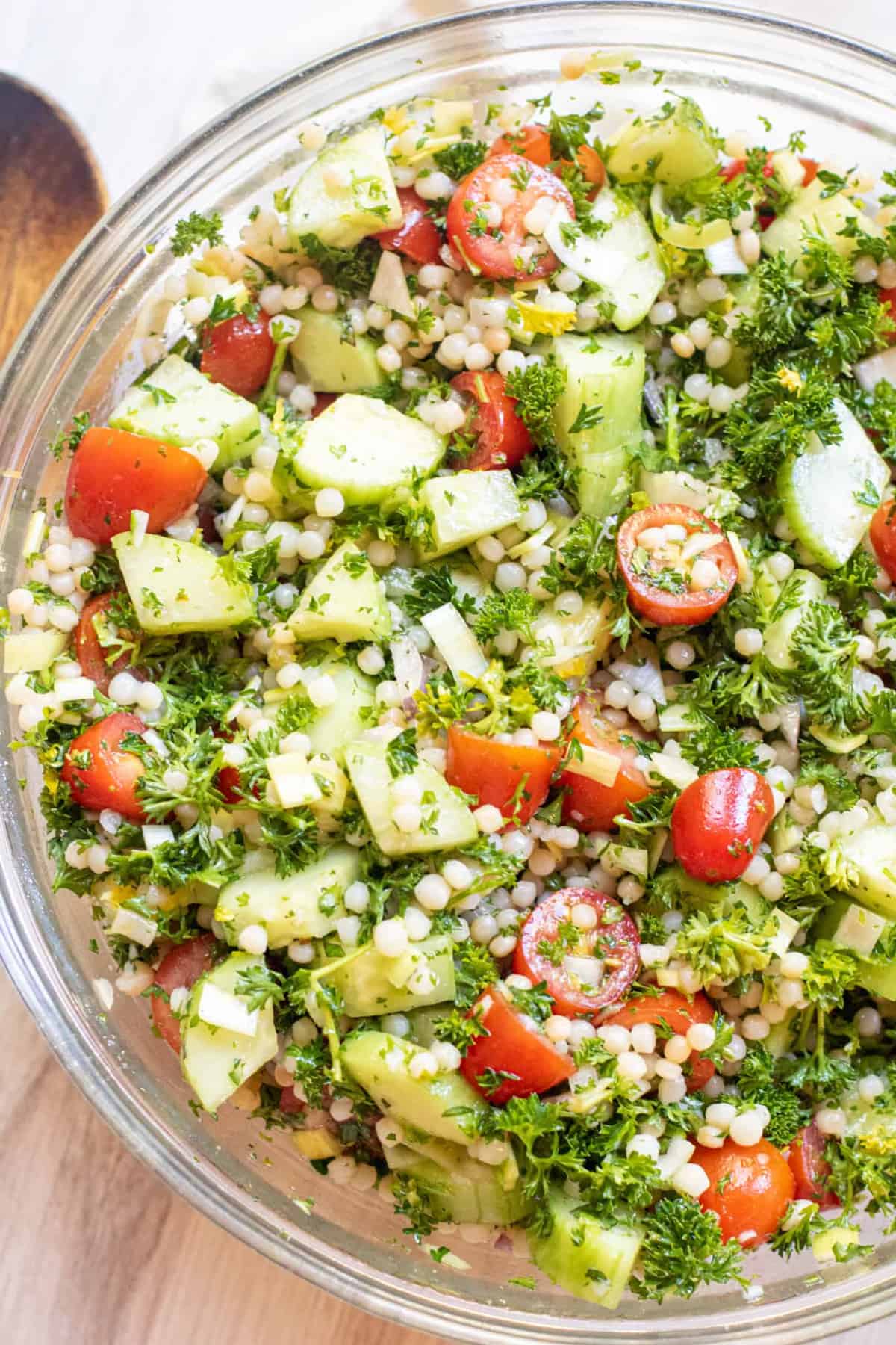 a bowl of couscous with tomatoes and cucumbers and parsley.