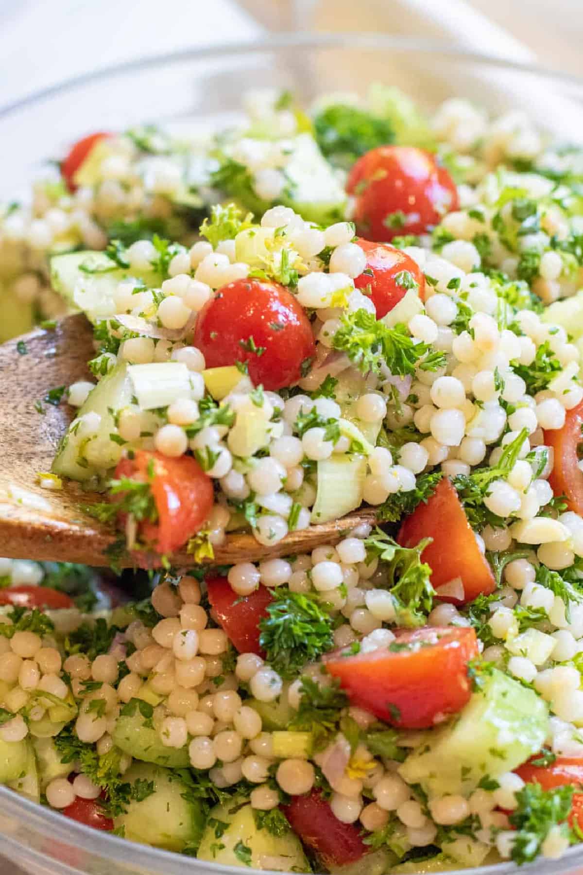 a wooden spoon holding some couscous with tomatoes and cucumbers.