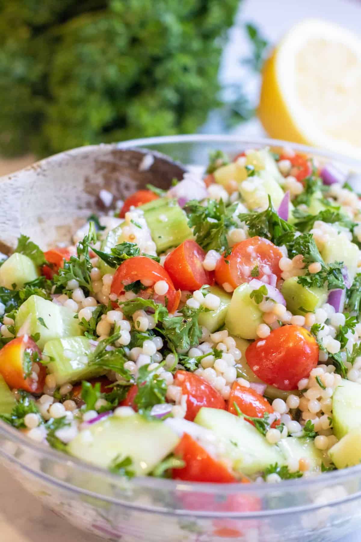 a bowl of couscous with tomatoes and cucumbers and parsley.