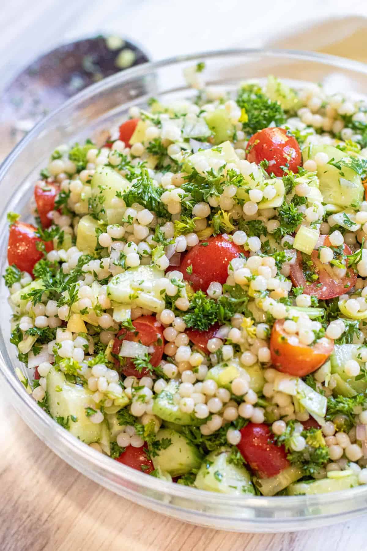 a bowl of couscous with tomatoes and cucumbers and parsley and Pinterest pin text.