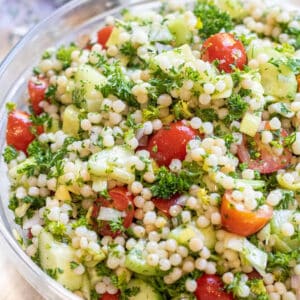 a bowl of couscous with tomatoes and cucumbers and parsley.