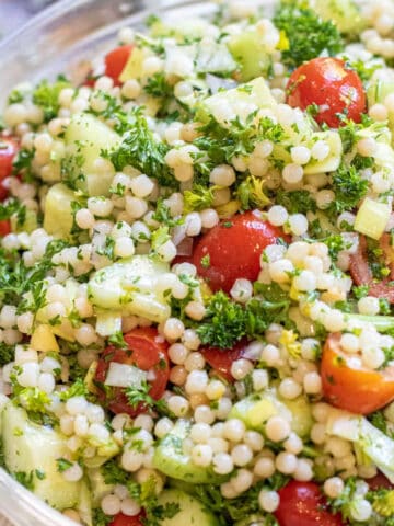 a bowl of couscous with tomatoes and cucumbers and parsley.