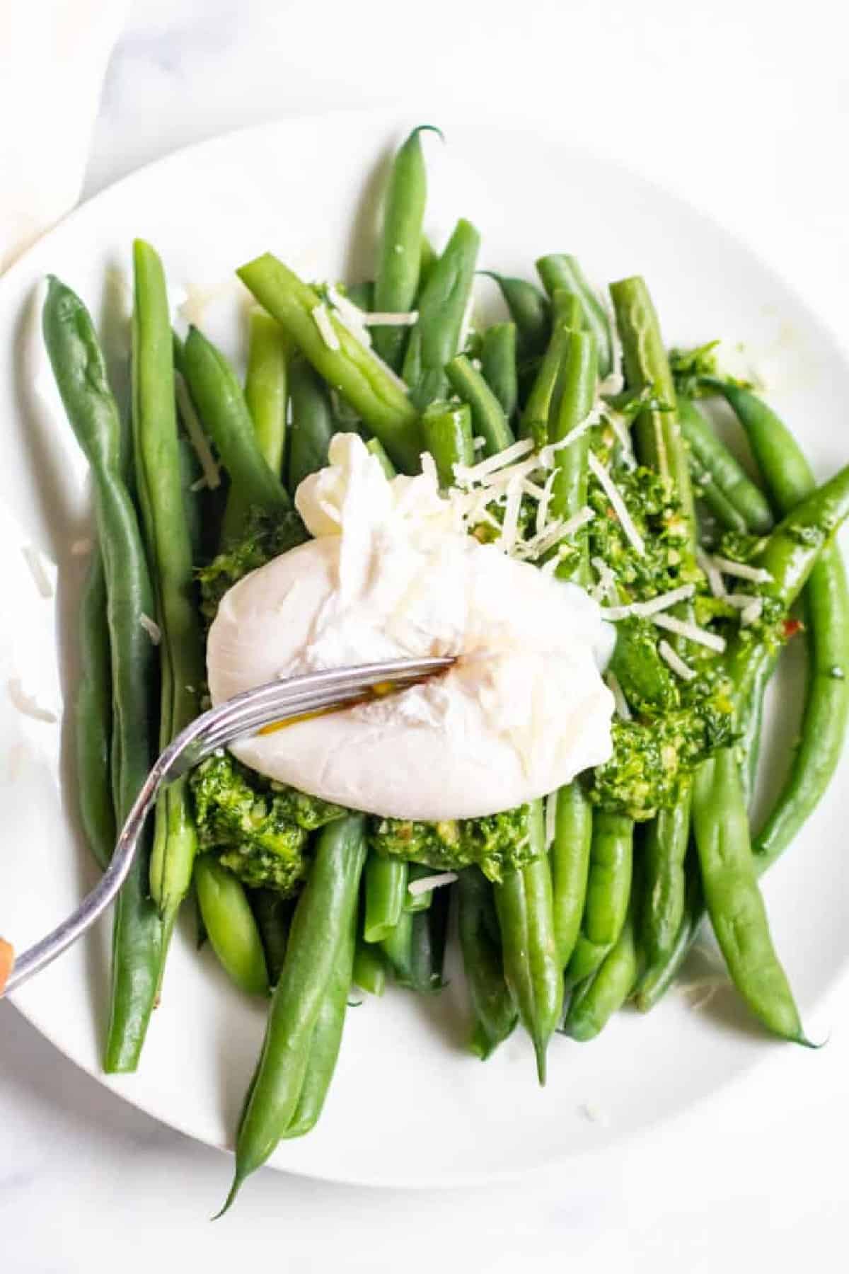two plates with green beans and pesto and topped with a poached egg.