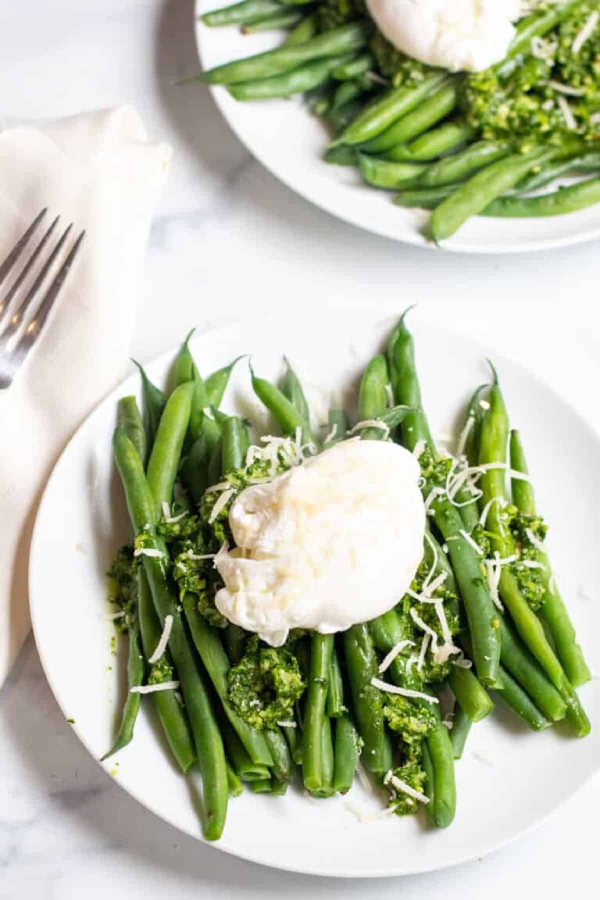 two plates with green beans and pesto and topped with a poached egg.