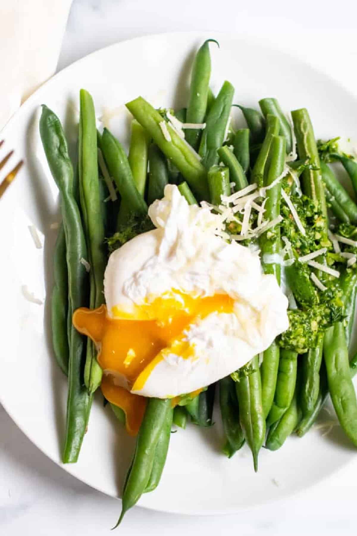 two plates with green beans and pesto and topped with a runny poached egg.