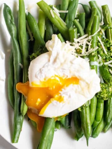 two plates with green beans and pesto and topped with a runny poached egg.