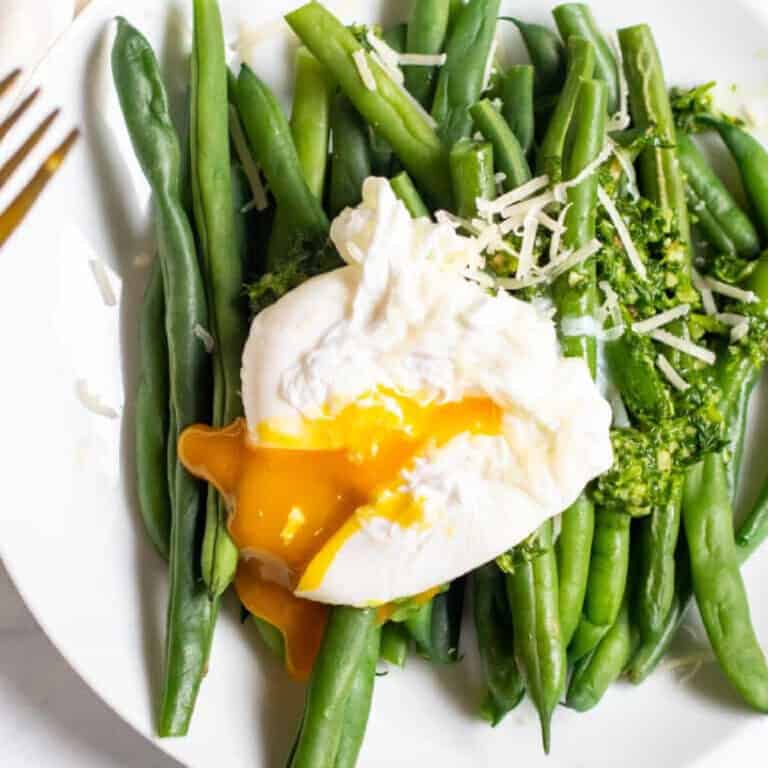 two plates with green beans and pesto and topped with a runny poached egg.