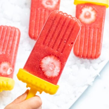 a small hand holding a strawberry popsicle.