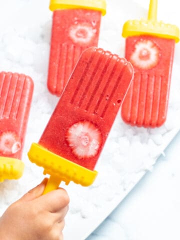 a small hand holding a strawberry popsicle.