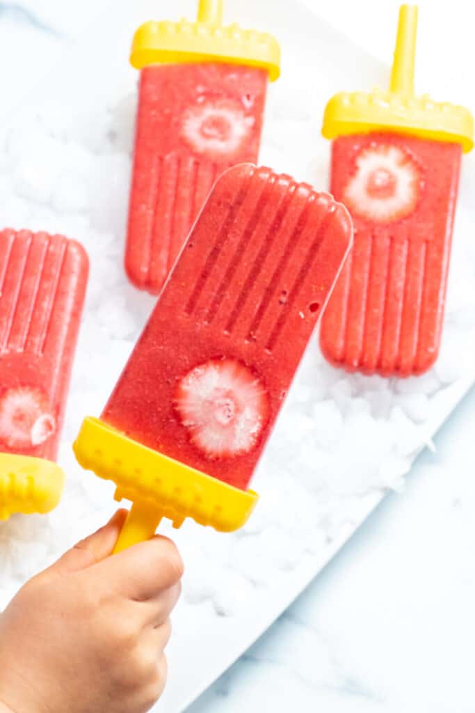 a small hand holding a strawberry popsicle.