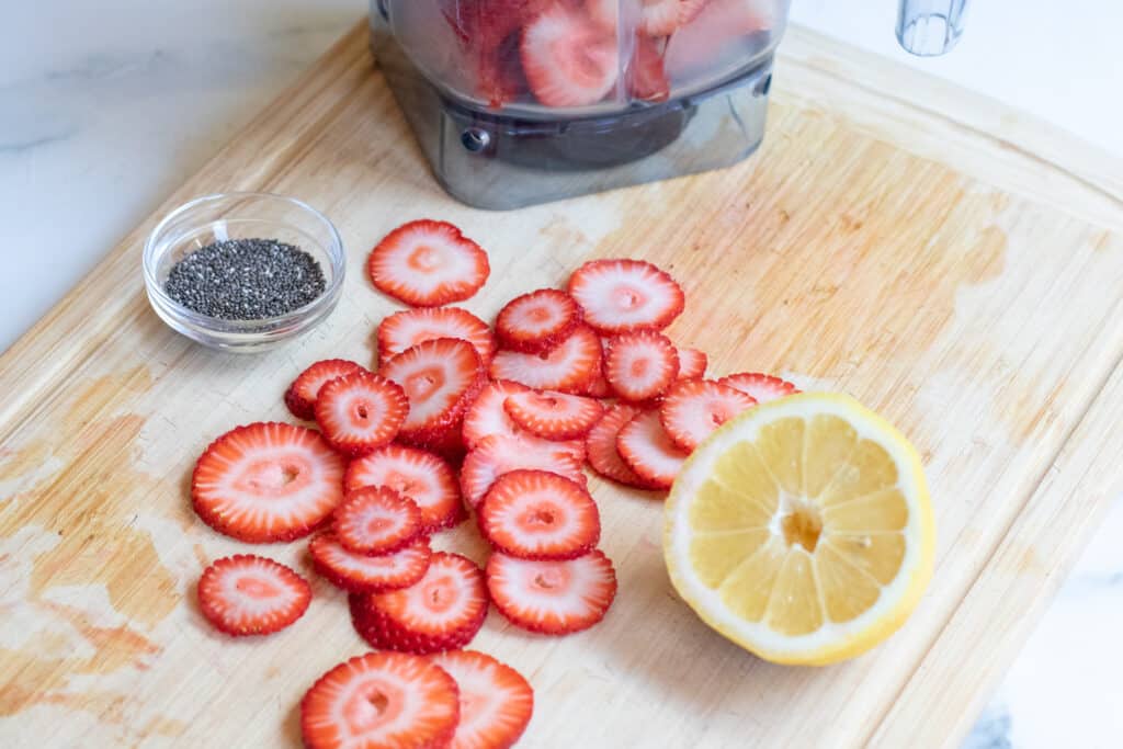 sliced strawberries, a halved lemon, chia seeds on a cutting board.