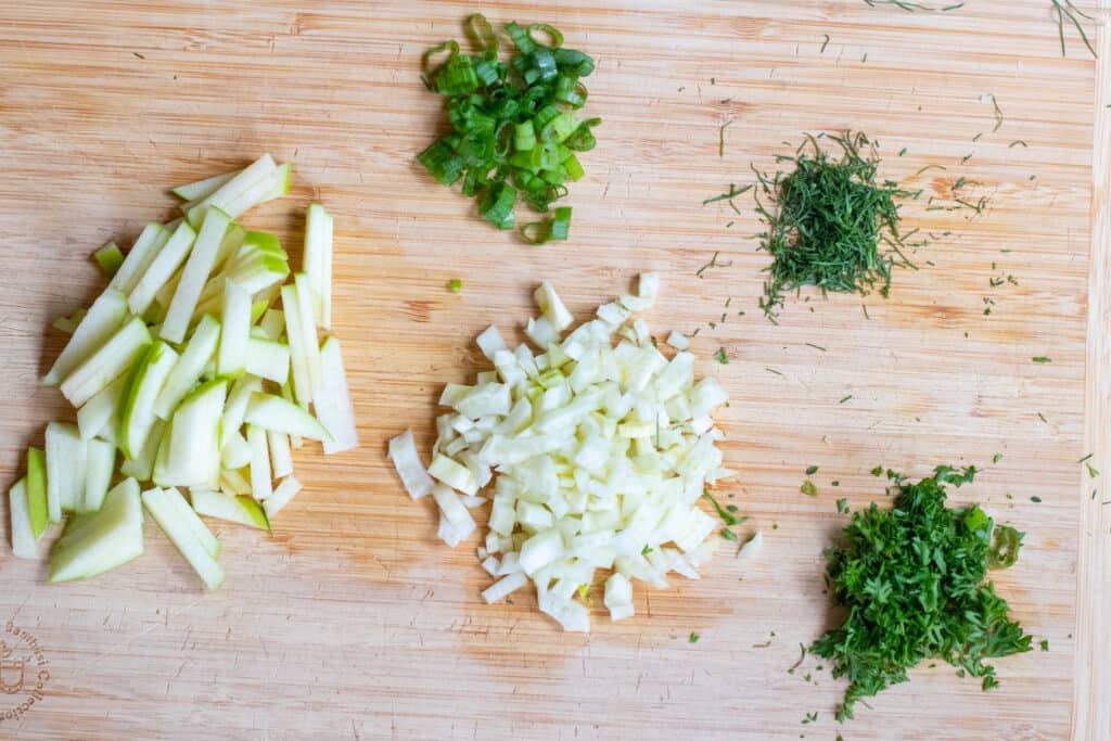 sliced apple, fennel, herbs on a cutting board.