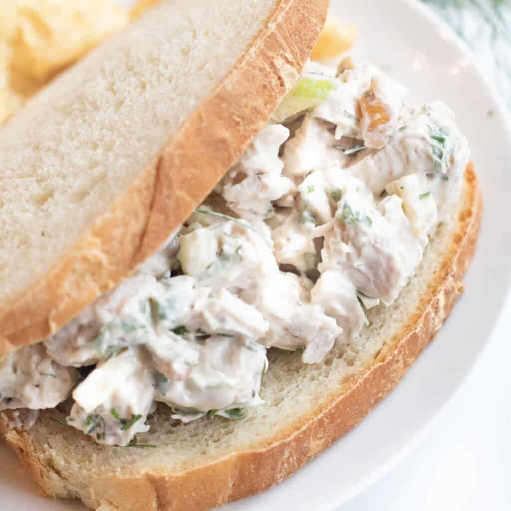 a close up of a creamy chicken salad in between two slices of white bread.
