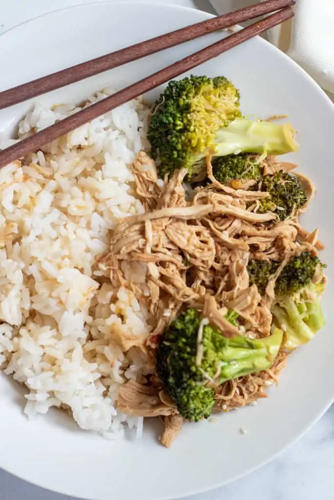 a plate with chopsticks, rice, and shredded chicken and broccoli.