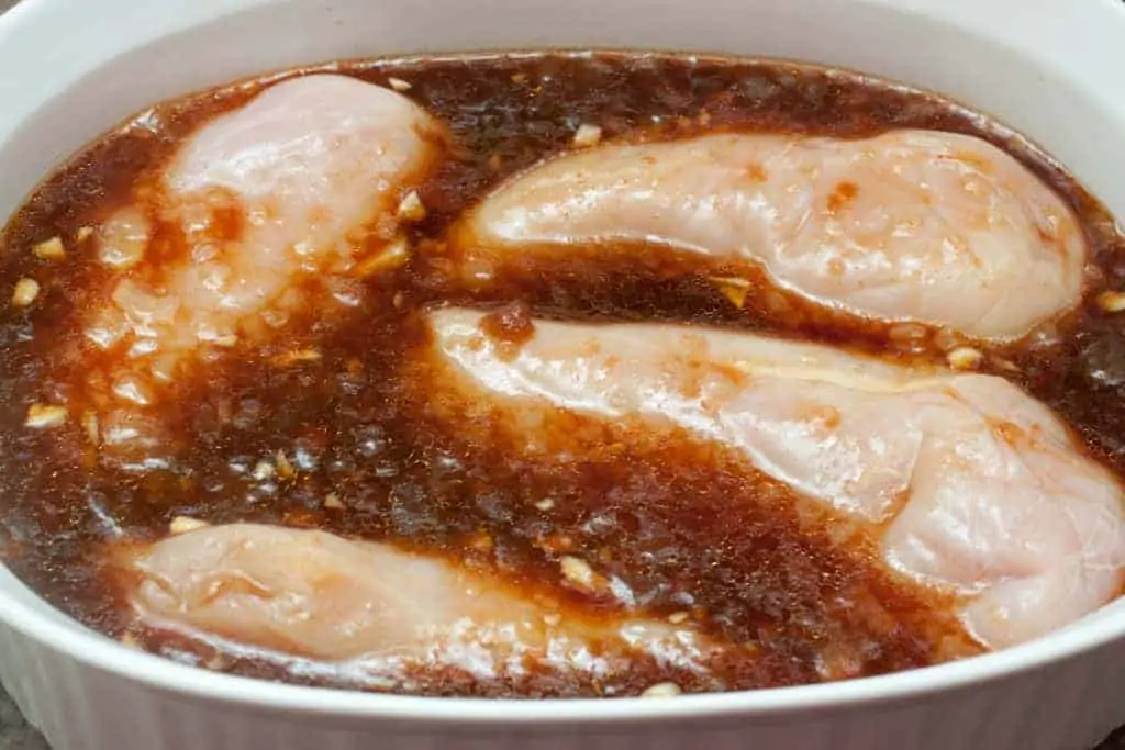 raw chicken breasts marinating in a daark sauce.