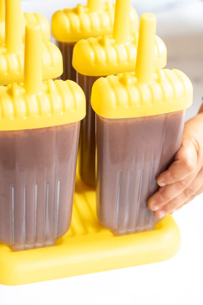 chocolate fudgesicles in molds with a toddler hand grabbing.